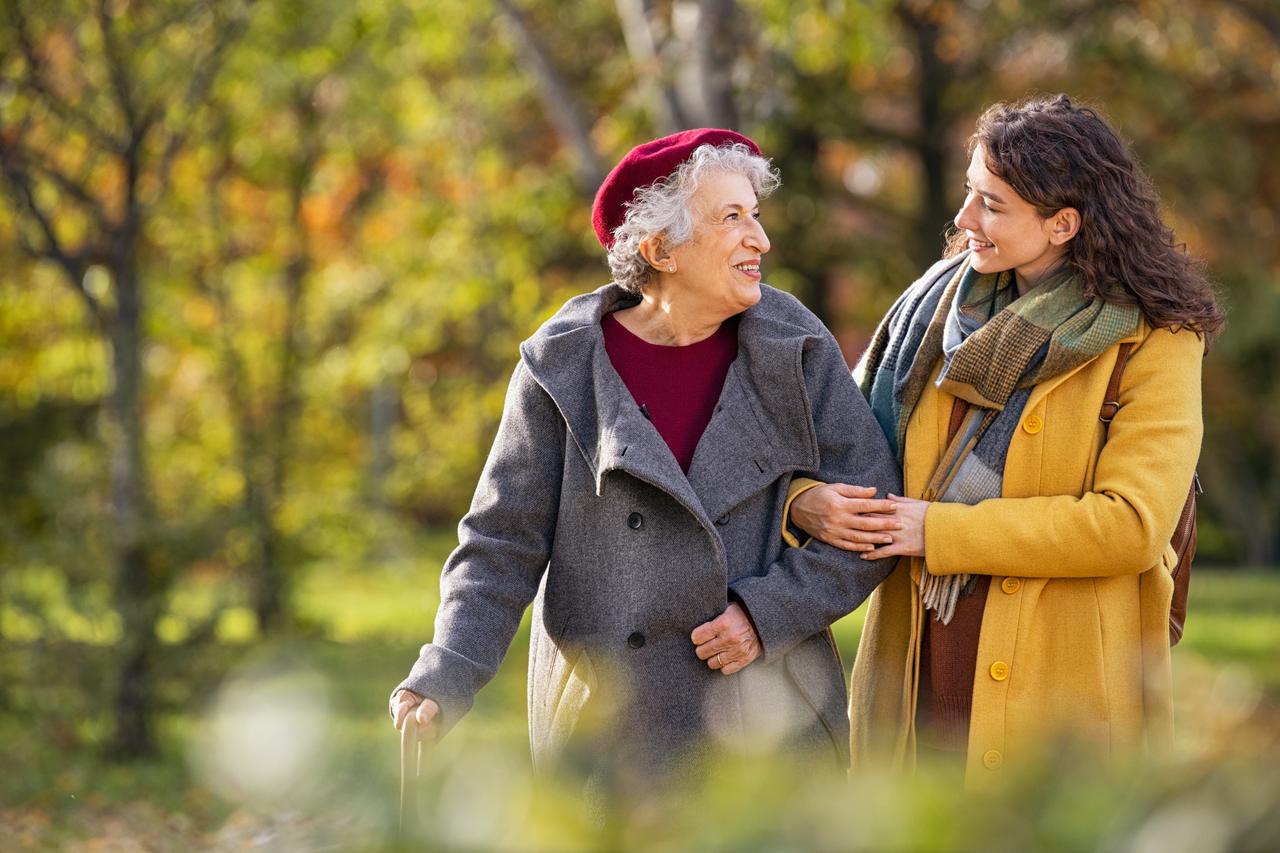 An adult walking arm in arm with an older parent outdoors.