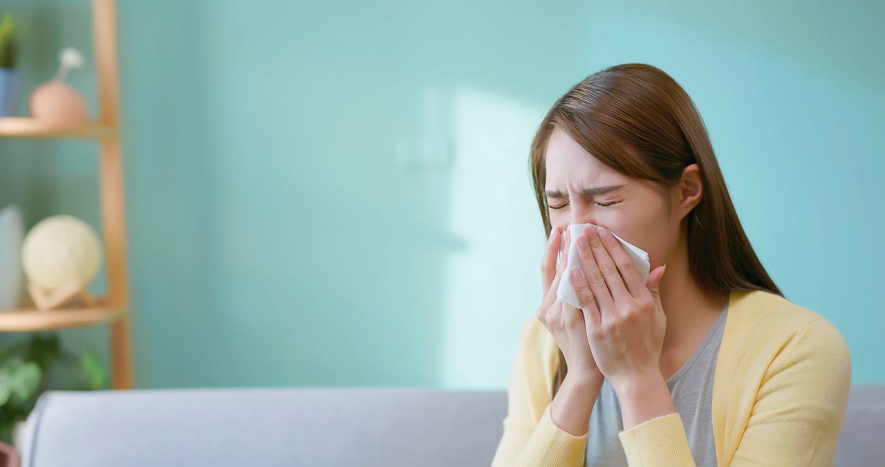 A person sneezing into a tissue at home during allergy season.